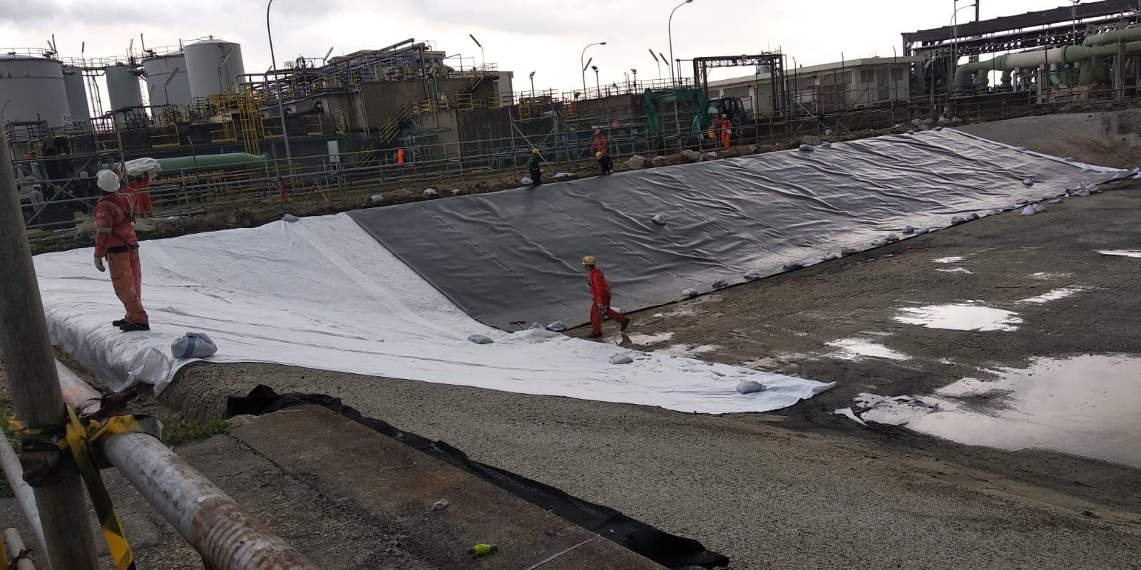 Stormwater crew deploying geomembrane across a containment basin on Jurong Island